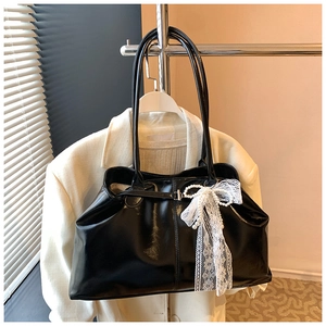 Detail of black glossy tote bag with lace bow and pearls on white suit background
