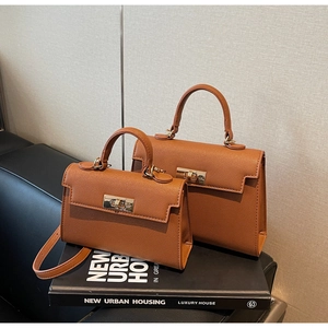 Macro detail of caramel brown leather texture and golden metal swivel lock on the Kelly bag