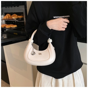 Dettaglio di borsa a mezzaluna bianca in pelle con logo dorato e ciondolo in metallo