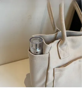 Detail of canvas tote bag side pocket holding a cosmetic bottle for storage utility