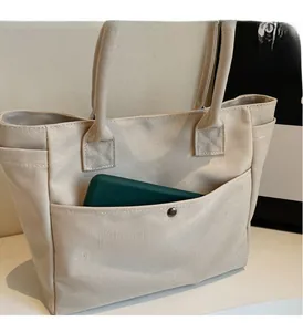 Close-up of beige canvas tote bag showing durable front pocket with metal buckle detail