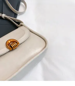 Detail view of cream saddle bag featuring vintage gold metal buckle and textured leather finish
