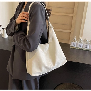 Close-up of a white textured leather tote bag with a wide shoulder strap worn by a model