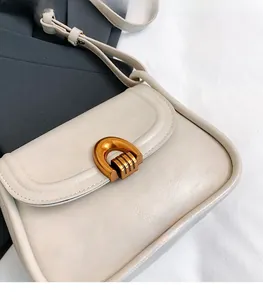 Macro detail of creamy saddle bag with vintage golden horseshoe buckle and textured leather
