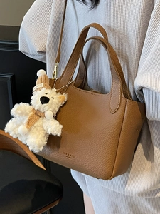 Brown lychee leather bucket bag with plush bear charm and adjustable shoulder strap