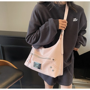 Sac demi-lune en cuir mat rose avec clous argentés et logo porté à l'épaule par un mannequin