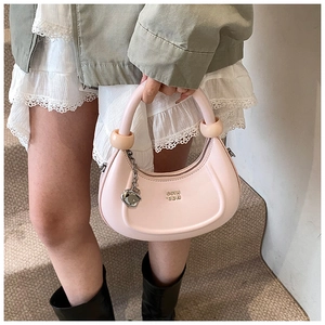 Borsa a mezzaluna rosa con catena in metallo e sfere decorative su cappotto verde