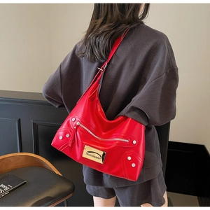 Détail d'un sac hobo en cuir rouge avec rivets argentés et plaque logo Noronoro en métal