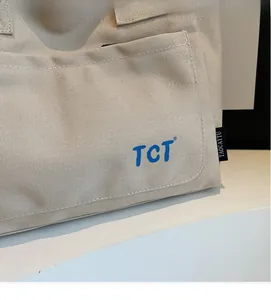 Close-up of beige canvas tote bag showing the front pocket, blue TCT logo and neat stitching
