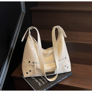 Détail du sac hobo beige avec clous argentés et pompon sur des livres noirs