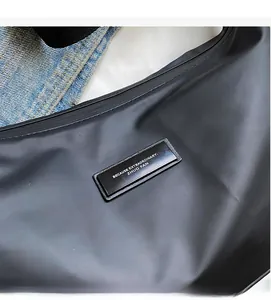 Detail shot of black nylon dumpling bag featuring a decorative logo plaque and matte texture