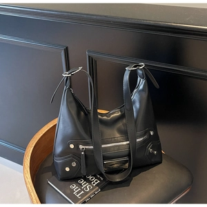 Détail d'un sac en cuir noir mat avec rivets métalliques argentés et plaque