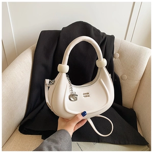 Dettaglio della borsa a mezzaluna in pelle PU crema con pendente G dorato e logo in metallo