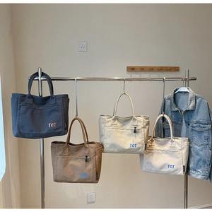 Detail view of TCT canvas tote bags in various colors hanging on a metal rack