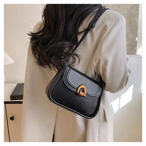 Detail of minimalist black leather saddle bag with gold horseshoe buckle on model