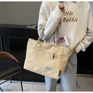Detail view of beige canvas tote bag with front pocket showing a magazine inside