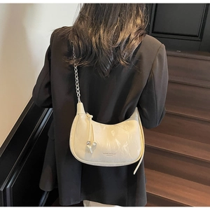 Détail d'un sac demi-lune crème avec bandoulière chaîne argentée et breloque nud