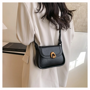 Model wearing a black leather saddle bag with a gold horseshoe buckle in a minimal room