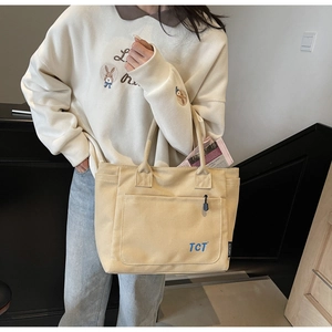 Detail of canvas tote bag showing front zipper pocket with TCT logo and sturdy handles