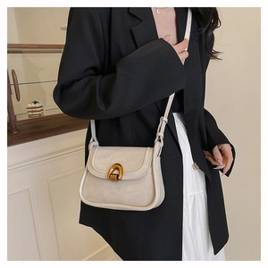 Detail of minimalist cream saddle bag with distinctive golden arch metal clasp and strap