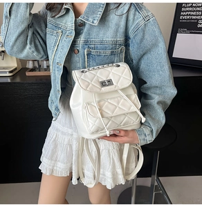 Detail of white quilted mini backpack with chain strap and metal lock in a street setting
