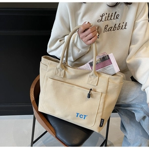 Detail of beige canvas tote bag showing side brand label and front zipper pocket detail