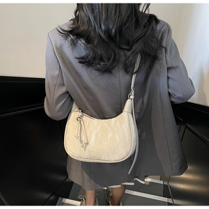 Détail du sac croissant blanc cassé avec texture plissée et breloque en métal chic