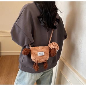 Detail of a handmade pink crochet sheep crossbody bag worn by a model in a cozy room