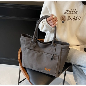 Close-up of durable gray canvas tote bag featuring large front pocket and orange logo