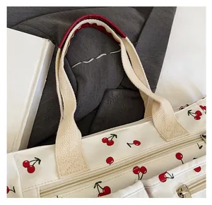 Detail of canvas tote bag showing cherry print, top zipper, and comfortable red handle pad