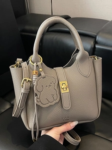 Sac seau élégant en cuir gris avec détails dorés et breloque chien tenu à la main