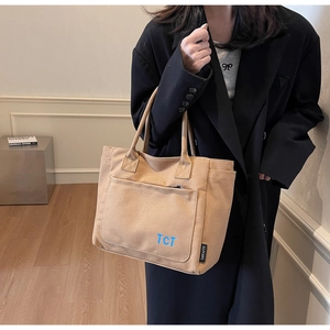Close-up of khaki canvas tote bag with front pocket and blue TCT logo for daily use