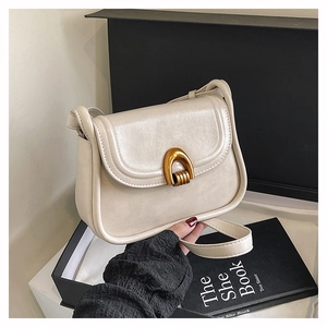 Detailed view of cream saddle bag with vintage gold horseshoe buckle and smooth texture