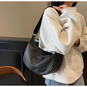 Detail view of black nylon crescent bag featuring a brand plaque and adjustable strap