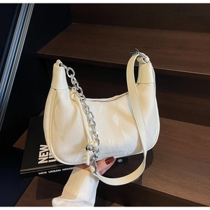 Détail d'un sac demi-lune blanc avec chaîne argentée posé sur des marches en bois