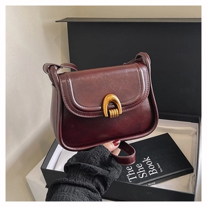 Detailed view of vintage burgundy leather saddle bag with golden horseshoe metal clasp