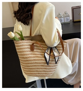 Detail of striped straw tote bag featuring leather straps and decorative slogan silk scarf