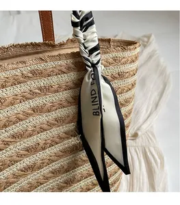 Close-up of bohemian woven straw tote bag featuring decorative black and white silk ribbon