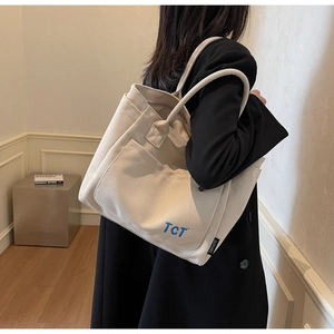 Detailed view of cream canvas tote bag with blue TCT lettering and large front pocket