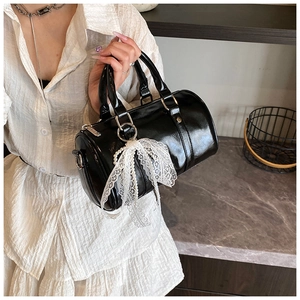 Detail of glossy black Boston bag featuring elegant white lace bow and pearl charm
