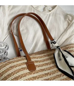 Detail of woven straw tote bag with brown leather handles and decorative silk scarf