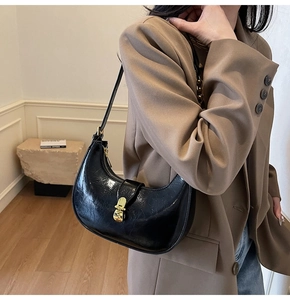 Close-up of black patent leather crescent bag with elegant gold metallic clasp closure