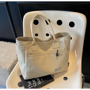 Detail of beige canvas tote bag with spacious front pocket and signature blue TCT logo