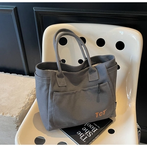 Close-up of grey canvas tote bag with orange TCT embroidery on a minimalist white chair