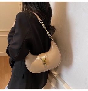 Beige patent leather crescent bag worn by model featuring gold chain and lock detail