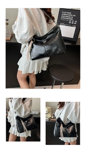 Detail of black glossy hobo bag with braided fringe pendant and sleek leather strap