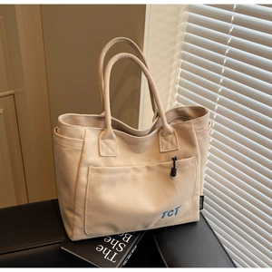 Detail of beige canvas tote bag featuring front pocket with blue TCT lettering