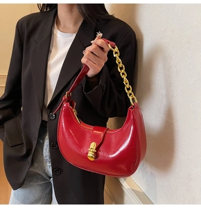 Detail of red glossy crescent bag with gold chain strap on black blazer jacket