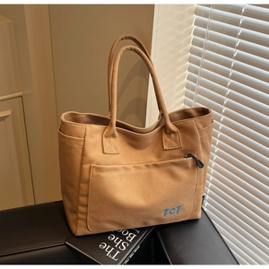 Detail of a large brown canvas tote bag with front zipper pocket and blue TCT logo