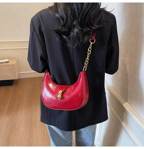 Detail of red crescent shoulder bag with glossy patent leather and gold chain strap